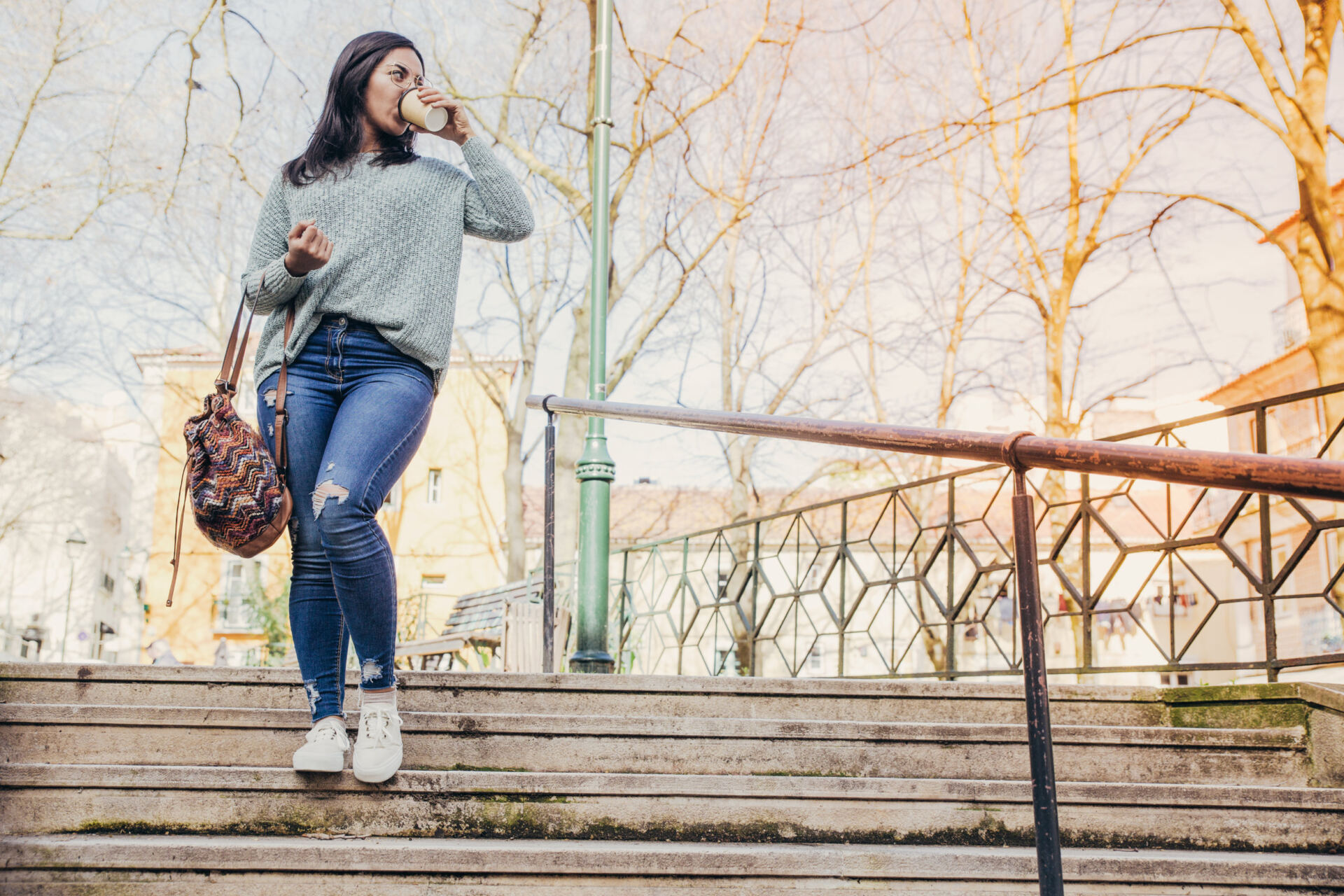 Young woman walking down city stairs and drinking coffee