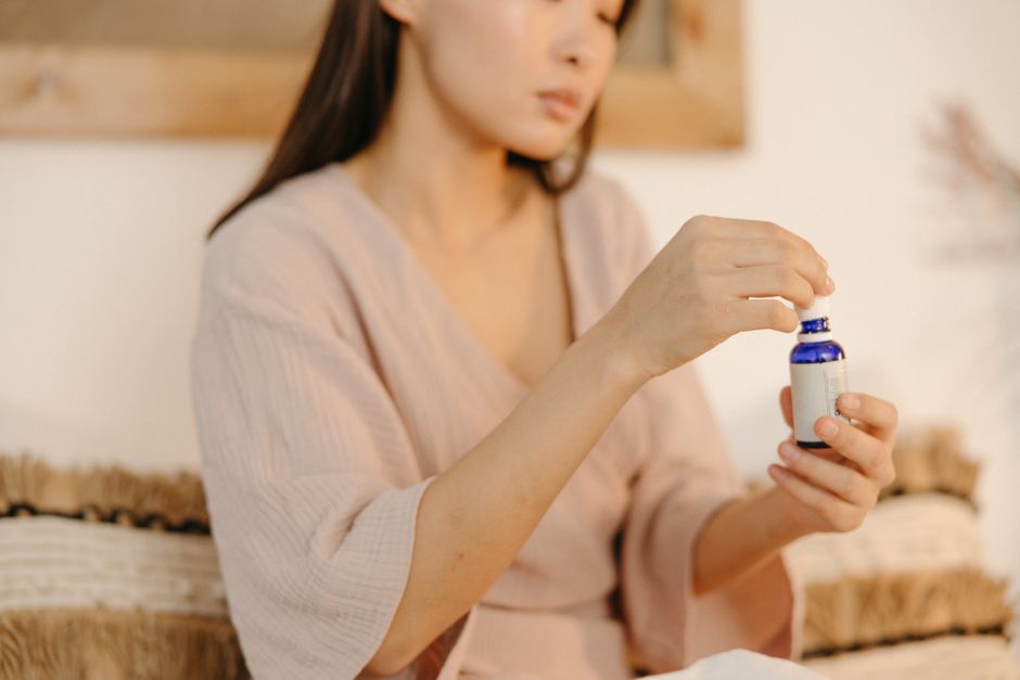 Asian woman opening a blue essential oil bottle indoors, emphasizing wellness lifestyle.