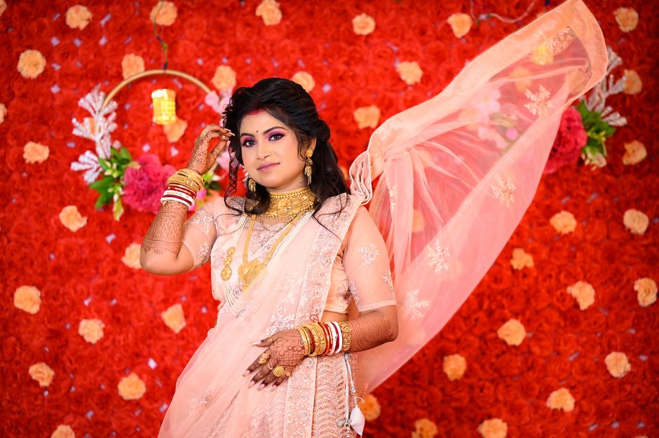 Stunning Indian bride in pink saree with henna tattoos against vibrant floral backdrop.