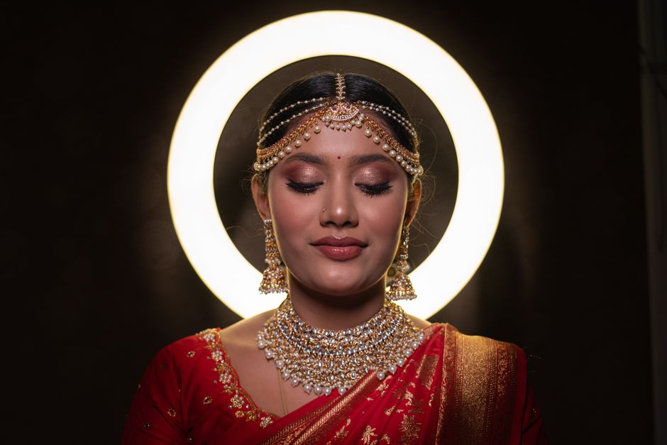 A beautiful Indian bride adorned in traditional red attire with exquisite jewelry, captured with a halo effect.