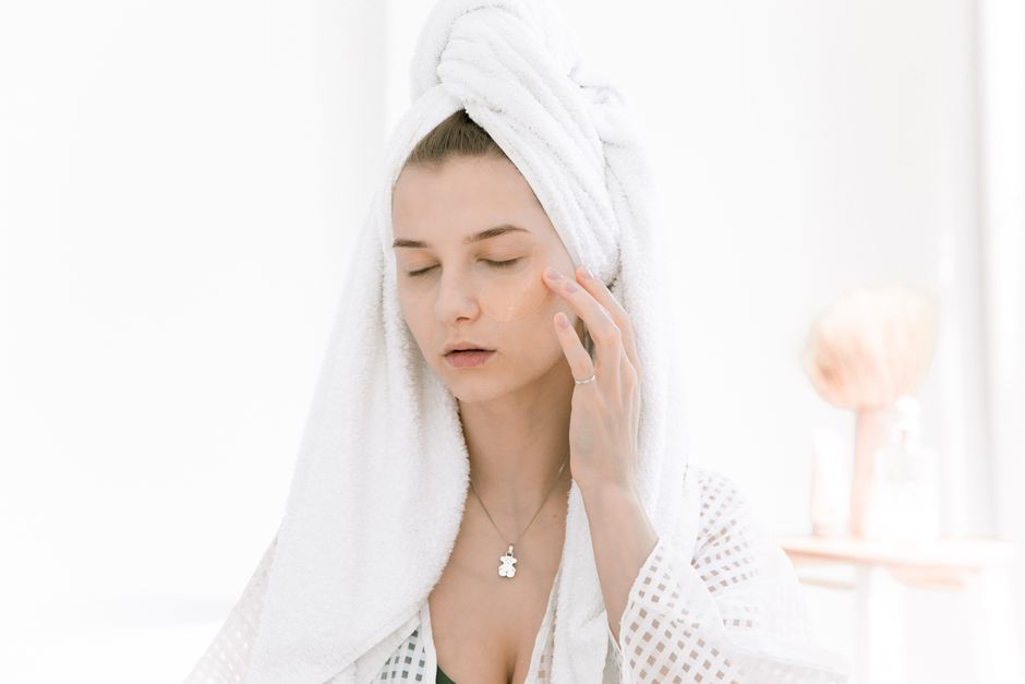 Woman in towel applying skincare indoors, enjoying a relaxing beauty routine.