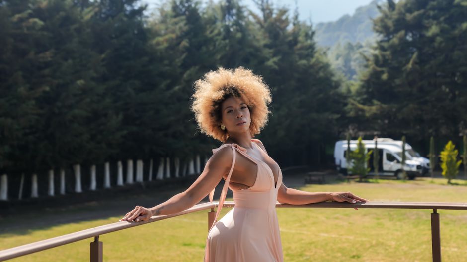 A woman with afro hair poses elegantly in a pink dress outdoors in Mexico.