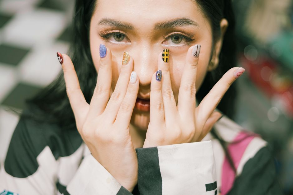 Close-up shot of a woman with colorful acrylic nails covering her face.