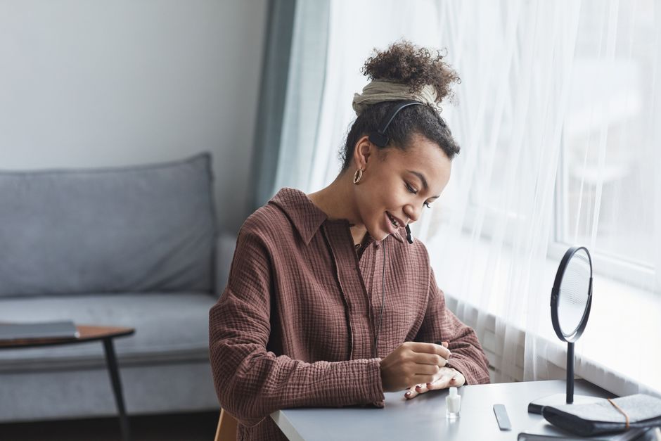 A woman multitasks by painting her nails while talking at her home office desk.