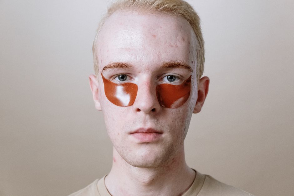 A man with orange eye patches looks directly at the camera, highlighting self-care and skincare.