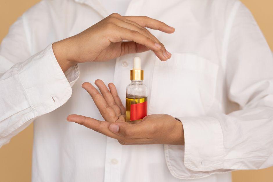 A person holding an essential oil bottle with a pipette against a neutral background. Skincare concept.