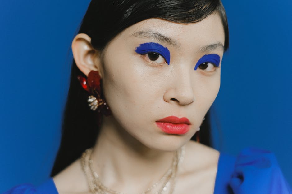 Striking close-up portrait of a woman with bold blue makeup against a blue background.