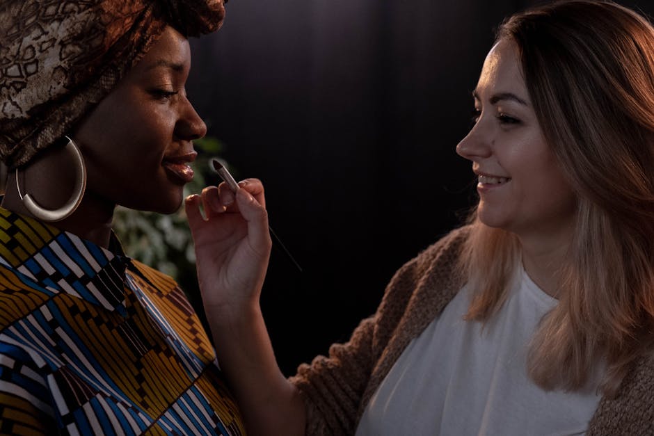 A makeup artist applying lipstick to a woman wearing a colorful turban and large earrings.