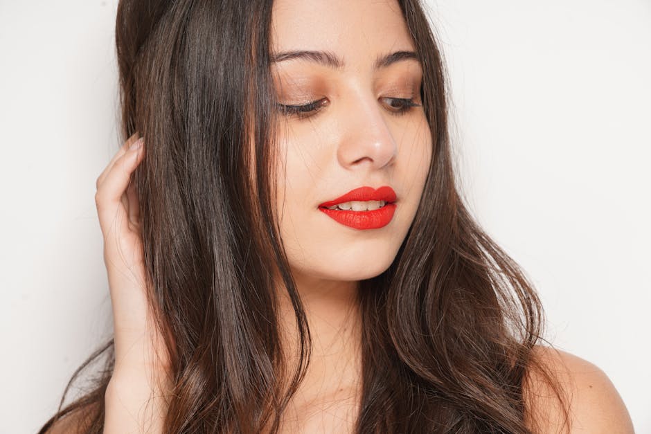 Close-up portrait of a woman with red lips and long brown hair against a white background.