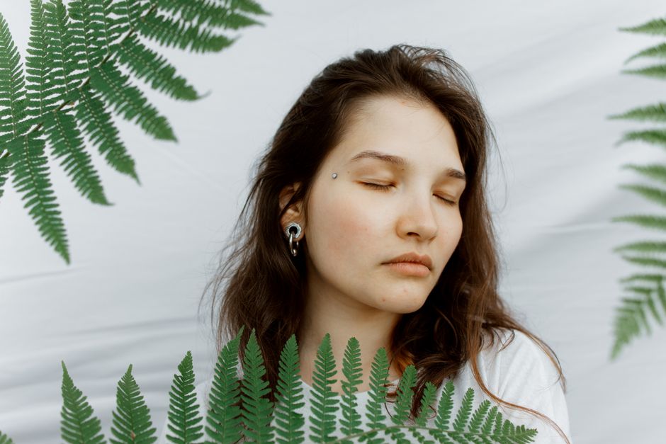 A tranquil portrait of a woman surrounded by ferns, shot against a white backdrop.