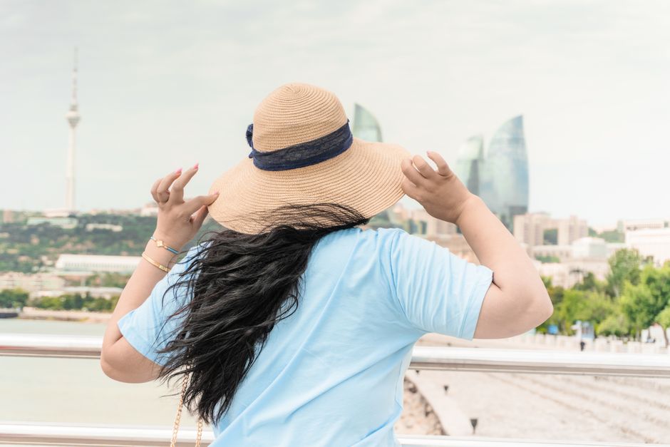 A woman with a hat admiring the Baku skyline, featuring iconic Flame Towers and TV Tower.