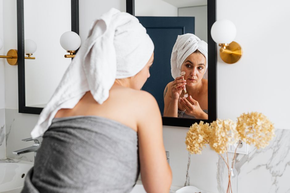 A woman uses a facial roller for skincare in a modern bathroom setting, embracing self-care.