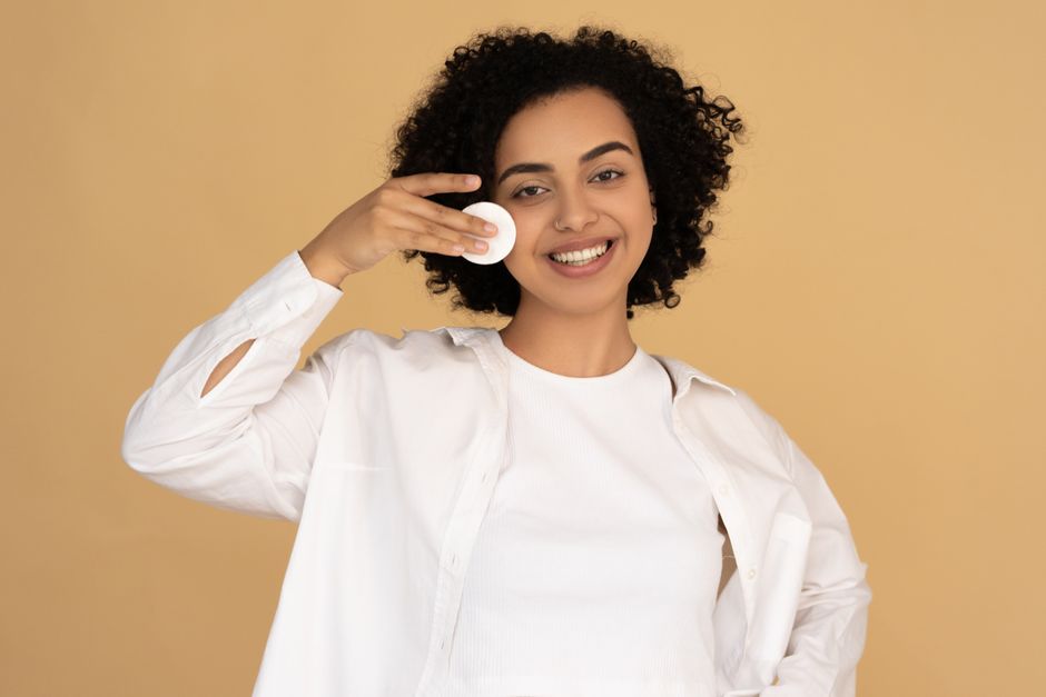 A cheerful woman applies skincare with a cotton pad, promoting healthy skin.