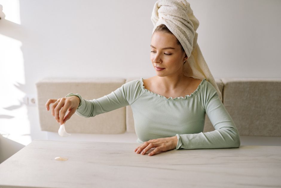 Woman with head towel applying eye patches during morning skincare routine indoors.