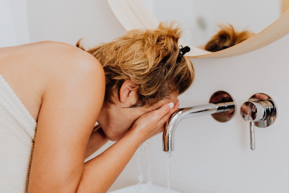 Adult woman washing her face at a modern bathroom sink during the morning routine.
