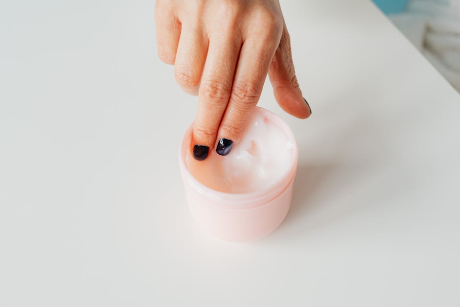 Close-up of a hand with painted nails dipping into a jar of face cream, representing self-care.