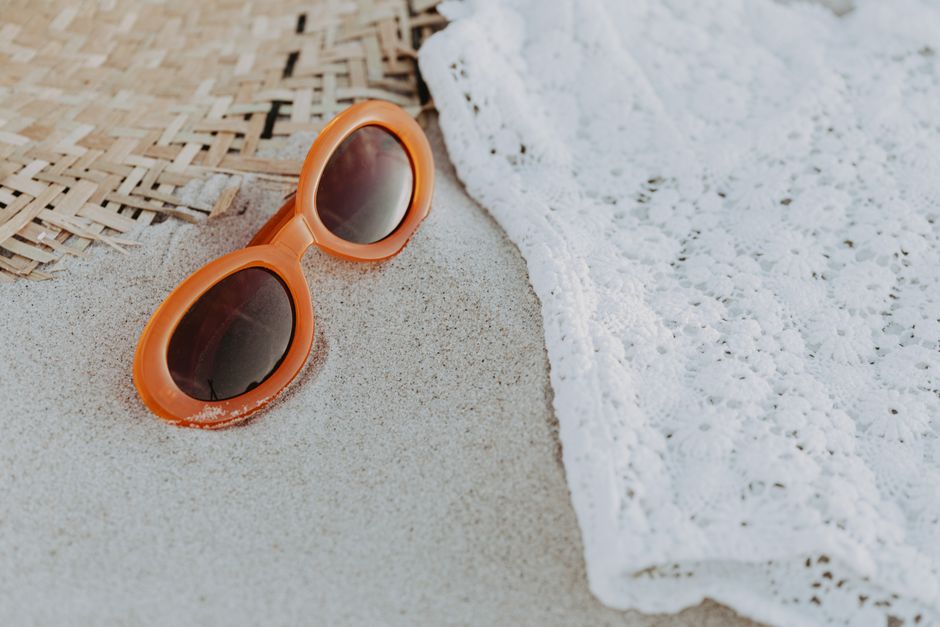 Orange sunglasses and lace fabric on beach sand - summer vibe close-up.