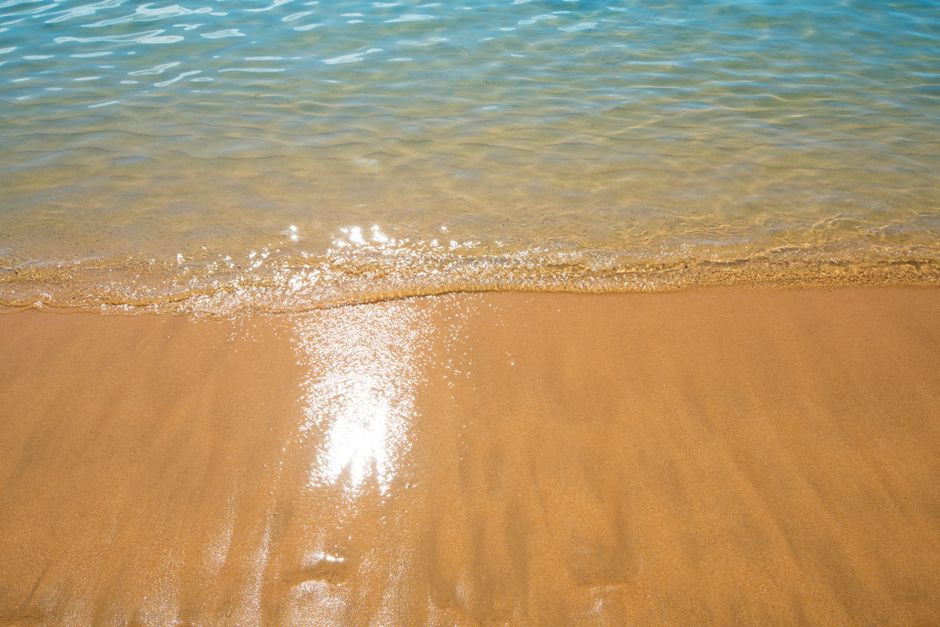 Experience the serenity of a golden sandy beach with gentle waves and warm sunlight.