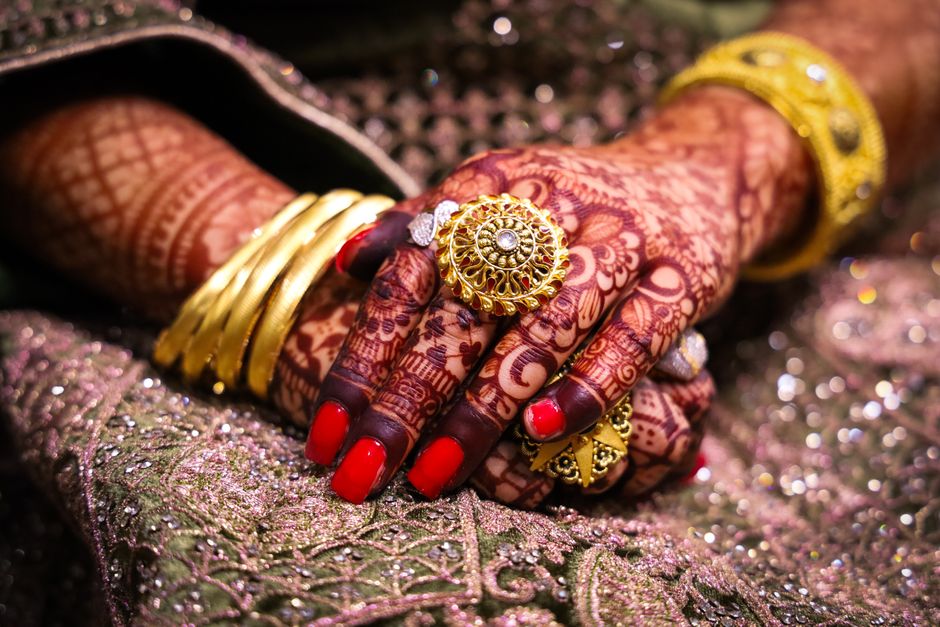 Close-up of beautifully hennaed hands adorned with traditional gold jewelry and vibrant fabrics.