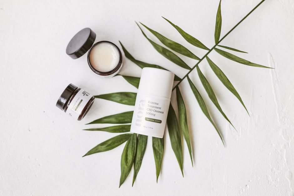 Minimalist product shot of CBD ointment and leaf on white background.