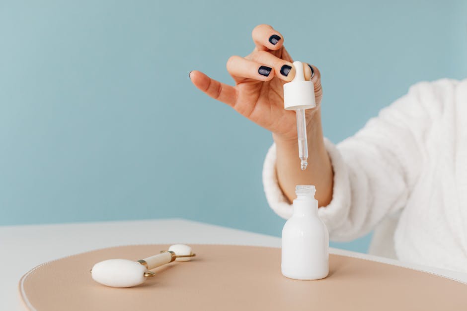 Hand in a bathrobe using a pipette to dispense skincare product into a white bottle.