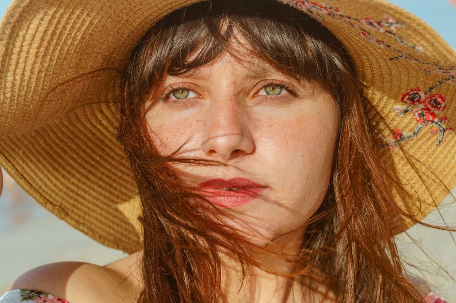Dreamy young female traveler with long hair in straw hat recreating on sandy beach on sunny day and looking away
