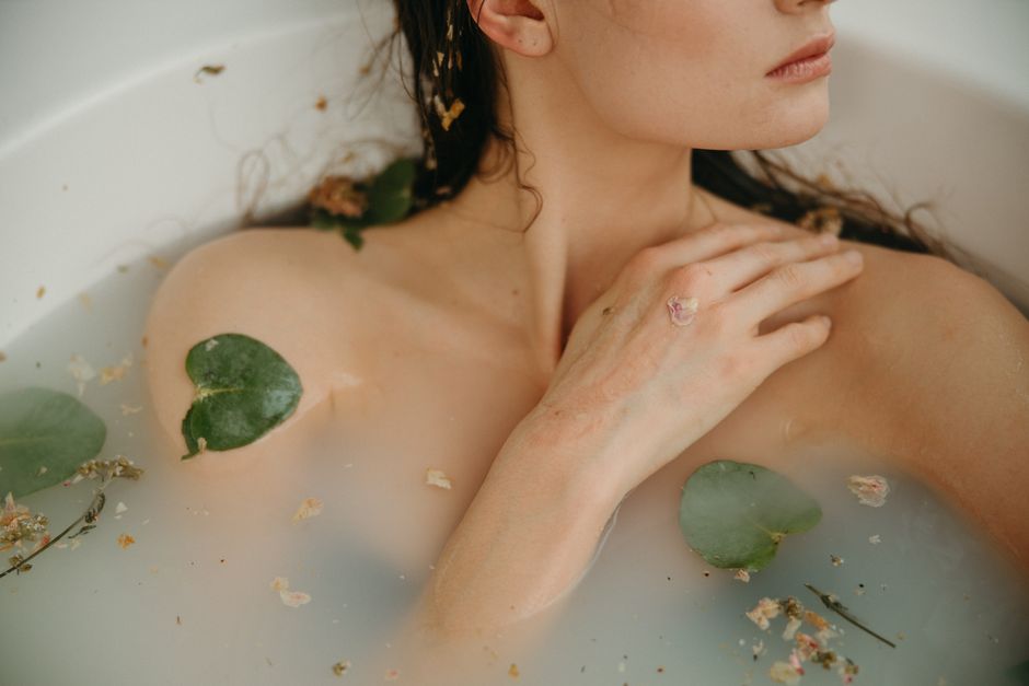 Woman relaxing in a serene bath with petals and leaves, promoting tranquility and self-care.