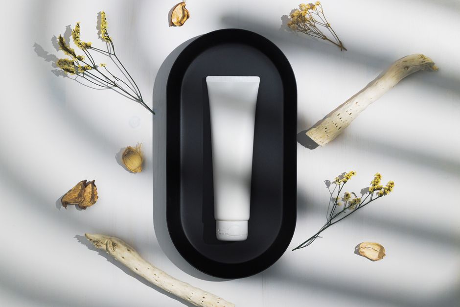 Elegant skincare tube on black tray surrounded by dried natural elements under soft shadows.