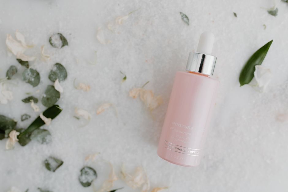High-quality product photography of a moisturizer dropper bottle on a floral and leafy background.