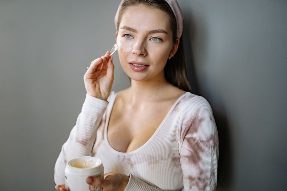 A woman in a headband applies skincare cream indoors, focusing on facial care and beauty routines.