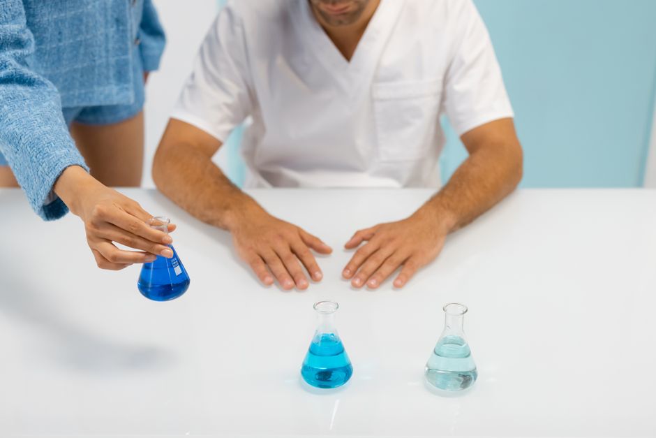 Hands conducting a laboratory experiment using Erlenmeyer flasks with blue liquid.