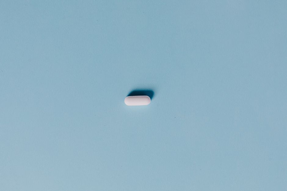 Single white pill on a blue background, representing medicine or healthcare.