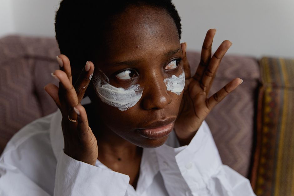 Close-up portrait of a woman applying face cream indoors, showcasing skincare routine.