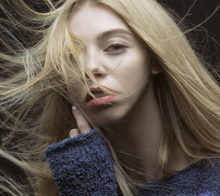 Close-up portrait of a woman with blonde, messy hair and a thoughtful expression, captured outdoors.