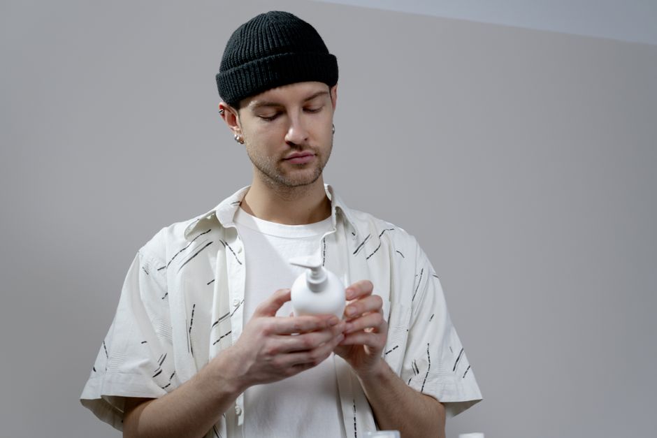 A young man examines a shampoo bottle in a modern indoor setting, wearing casual attire.