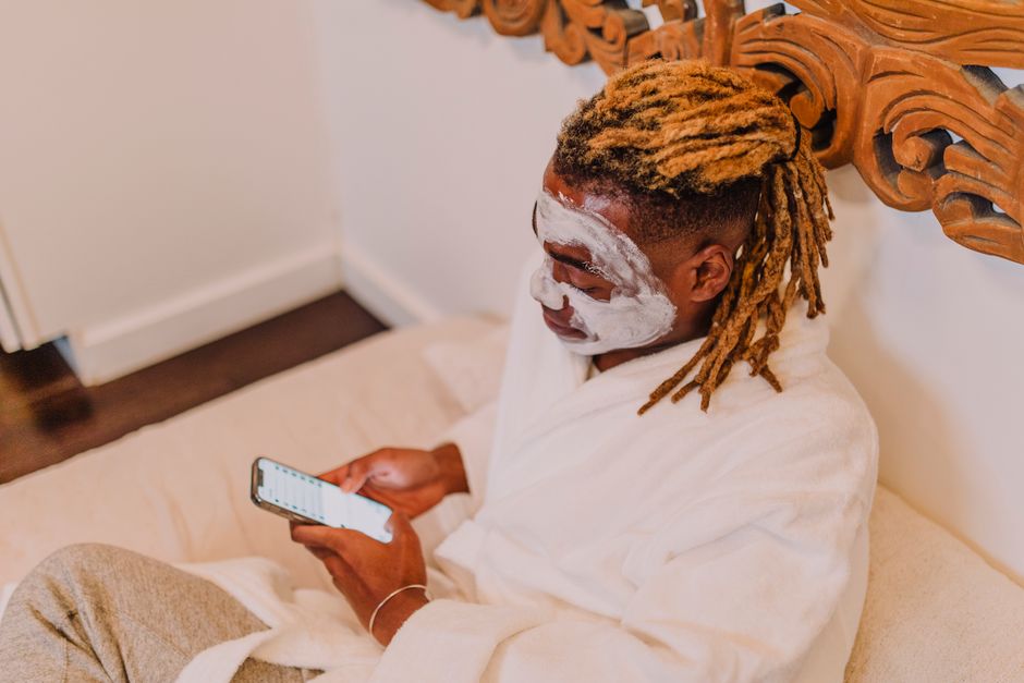 A man wearing a face mask enjoys a relaxing spa day at home, browsing on his phone.