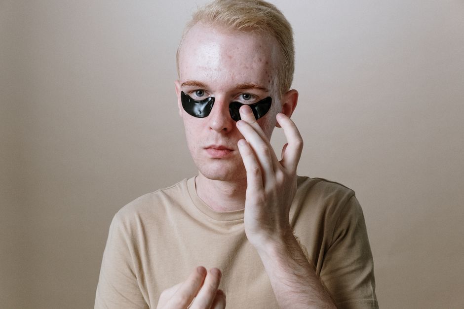 A young man applies under-eye patches for a refreshing skincare routine indoors.